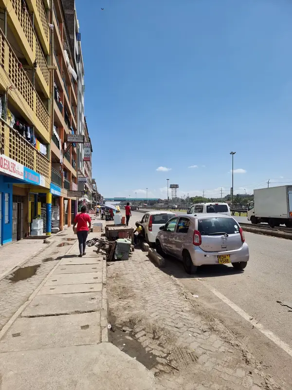 O stradă cu blocuri, mașini parcate și cer senin