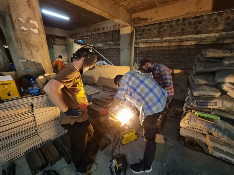 Doi oameni sudează, cu scântei, în atelier